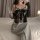 Woman wearing sexy lace lingerie set with sheer push-up bodysuit, holding a glass of champagne on a bed.