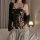 Woman in black lace lingerie set with sheer push-up bodysuit and uniform-style sleepwear, holding a glass.
