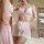 Woman wearing pink and white lace maid costume set with sheer mesh skirt, contrast trim, and bow details in elegant bedroom s...
