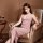 Woman in pink sheer lace mesh nightgown with side slit, seated elegantly on velvet armchair beside wine glass — seductive sle...
