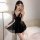 Woman in black lace peek-a-boo sleep dress with sheer skirt, posing by bed — seductive nightwear with open-crotch design.