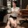 Woman in white lace secretary blouse and black skirt, kneeling by desk with id badge.