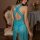 Woman wearing a backless, sheer turquoise nightgown with elegant cutouts and lace trim, seated on a vintage floral chair.