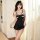 Woman modeling black lace sleep dress with bow detail and open-crotch design, sheer fabric, thin straps, pearl necklace, soft...