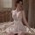 Woman wearing white lace sleep dress with push-up cami top and elegant trim, sitting on bed in soft lighting.