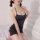 Woman modeling black sheer mesh bodysuit with open-crotch design and lace trim, posing on white bed for intimate at-home wear...
