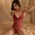 Woman wearing red lace teddy lingerie, sheer open-crotch design, posing seductively on bed with soft lighting.