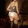 Woman wearing sexy leopard print lace bodysuit with underwire, open-crotch design, and black stockings in a dimly lit room.
