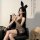 Woman in sexy leopard print lingerie set with bunny ears, posing seductively on black chair for role play.