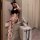 Woman in black maid lingerie bodysuit with cat ears, posing by a cabinet with a flower bag nearby.