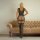 Woman wearing a sheer mesh bodysuit with cut-out details and an open-crotch design, standing in front of a beige tufted sofa.