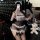 Woman in black and white lace maid lingerie set with garters, posing on leather couch.