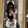 A person wearing a black and white maid costume with ruffles, bows, and paw prints, taking a mirror selfie.