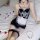 Woman in black and white sexy maid costume with lace trim, fishnet stockings, and rose petals on bed.