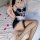 Woman in black and white lace maid costume with fishnet stockings, posing on bed with rose petals.