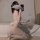 Woman kneeling on bed in white lace maid costume with sheer corset, bow ties, and stockings for role play lingerie.