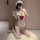 Woman in white lace maid costume with red bow, sheer stockings, and headpiece, kneeling on fluffy rug.