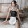 Woman in black pvc leather maid costume with white apron, fishnet stockings, and ruffled collar, posing on a fluffy rug for r...