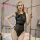 Blonde woman models a sheer black mesh bodysuit with patent leather trim, satin details, and a back zipper for nightclub wear...