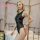 Blonde woman modeling a black mesh lace bodysuit with satin and patent leather accents, sheer shapewear nightclub outfit.