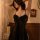 Woman wearing black mesh lace sleepwear set with sheer v-neck and front hook closure, posing in romantic bedroom setting.