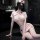 Woman in pink nurse costume with lace-up skirt and sheer stockings, posing seductively on dark marble floor.