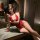 Woman wearing red lace open-crotch bodysuit, sheer temptation lingerie set, sultry pure outfit in elegant indoor setting.