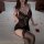Woman wearing black lace sleepwear set with deep v-neck bodysuit and elastic straps, seated on bed with rose petals.