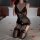 Woman in black lace bodysuit with deep v-neck and elastic straps, kneeling on bed with rose petals.