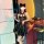 Woman in shiny black pvc catwoman costume with lace-up bodysuit, garter belt, cat ears, holding wine glass at bar.