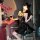 Woman in black pvc catwoman costume with lace-up bodysuit, garter belt, and thong lingerie, holding wine glass at bar.