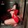 Woman in red ripped sheer mesh bodysuit with cut-outs, posing with whip and roses.