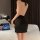 Woman wearing a black sheer lingerie skirt outfit, part of the sexy secretary bodysuit set, standing by a bed with a laptop.