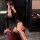 Woman in a sexy secretary costume outfit with a bodysuit for role play, sitting on a red stool and taking a mirror selfie.