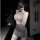 Woman in sheer gray bodycon skirt set with halter top, posing confidently in a dimly lit room.