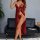 Woman wearing red sheer lace sleep dress with matching lingerie, posing elegantly beside black leather sofa in modern room se...