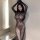 Woman wearing sheer black lace bodysuit with open-crotch design, posing indoors near window.