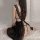 Woman wearing black sheer lace sleepwear with back slit, sitting on white bed. flirty mesh nightgown lingerie.