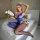 Woman wearing blue sheer mesh bodysuit with single-shoulder design, posing on bed holding white roses.