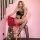Woman wearing a sexy sheer mesh bodysuit with single-shoulder design and open-crotch detail, posing on a pink stool.