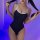 Woman wearing black sheer milk silk bodysuit with white trim, posing in purple-lit room.