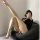 Woman in shiny black fishnet stockings with tear-away crotch, posing on bean bag in high heels.
