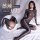 Woman modeling a shiny black open-crotch bodysuit with sheer mesh details and built-in sleeve, posing on a bed.