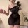 Woman wearing a shiny, sheer black lingerie dress with a backless design, holding a black rose and pearls.