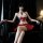 Woman in red and white pleated jk uniform set with bells, seated on black leather couch. premium adult costume for women.