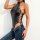 Woman wearing a sleek black pu leather bodysuit with side ties and halter neck, paired with blue jeans.