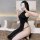 Woman wearing black high-slit cheongsam lingerie dress, backless design, posing on bed with phone covering face.