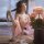 A woman elegantly poses beside a vase of pink flowers, wearing a delicate pink hanfu-inspired sleepwear set featuring an open...