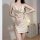 Woman wearing a cream satin slip dress with deep v-neck and sparkling chain side slit, styled as sexy sleepwear or secretary ...