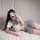 Woman in cute jk uniform-style short skirt with white top and bow, lying on bed, showcasing playful schoolgirl-inspired outfi...